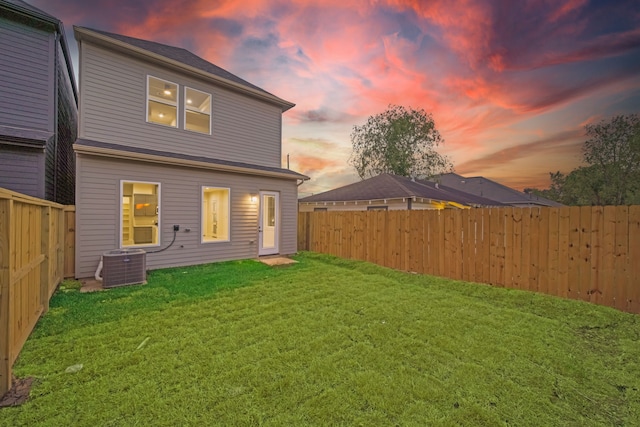 back house at dusk with a yard and central AC unit