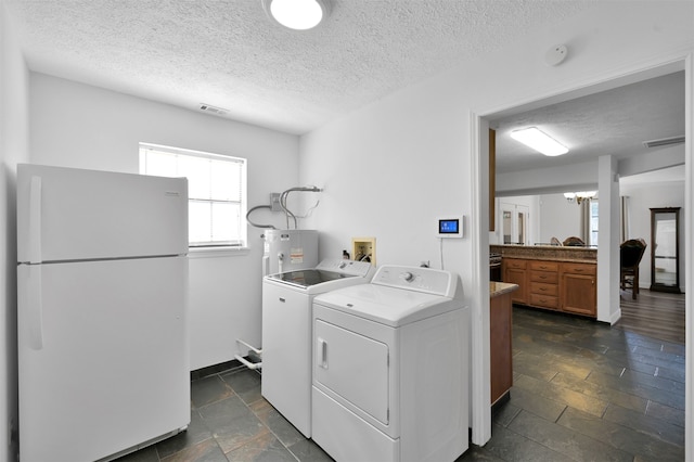 clothes washing area with washer and clothes dryer, electric water heater, a textured ceiling, and a notable chandelier