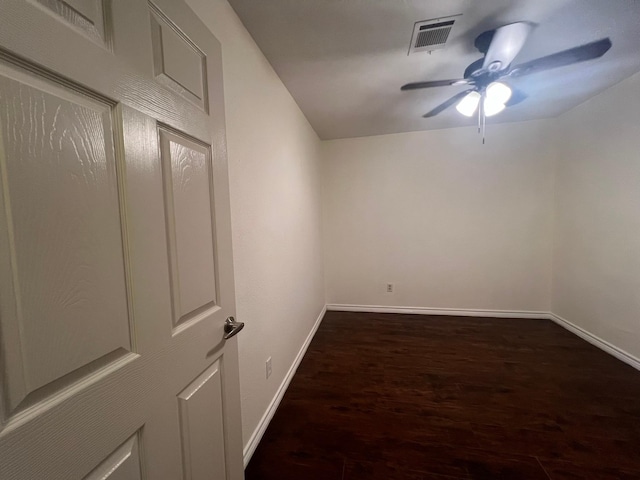 spare room featuring dark wood-style flooring, a ceiling fan, visible vents, and baseboards
