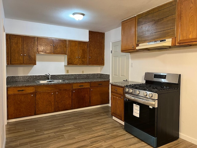 kitchen featuring stainless steel range with gas stovetop, a sink, dark wood finished floors, dark countertops, and under cabinet range hood