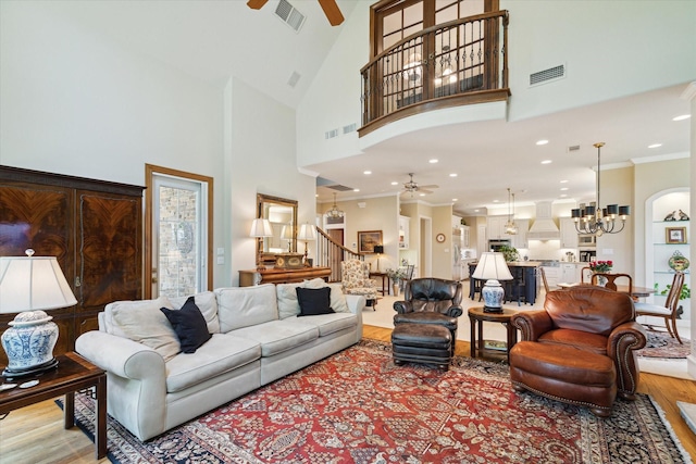 living room with light wood-type flooring, ceiling fan with notable chandelier, high vaulted ceiling, and ornamental molding