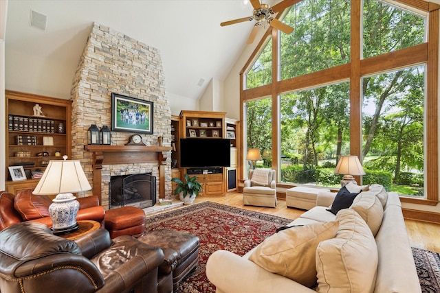 living room featuring high vaulted ceiling, hardwood / wood-style flooring, ceiling fan, built in features, and a fireplace