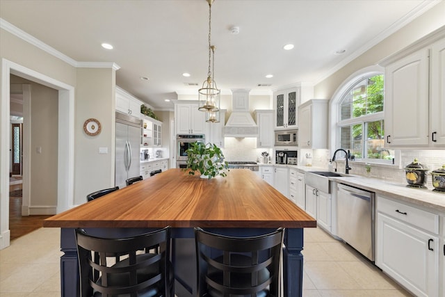 kitchen featuring a center island, built in appliances, custom range hood, butcher block countertops, and white cabinetry