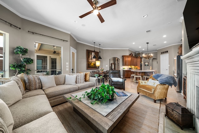 living room with ceiling fan with notable chandelier, a premium fireplace, light tile patterned floors, and crown molding