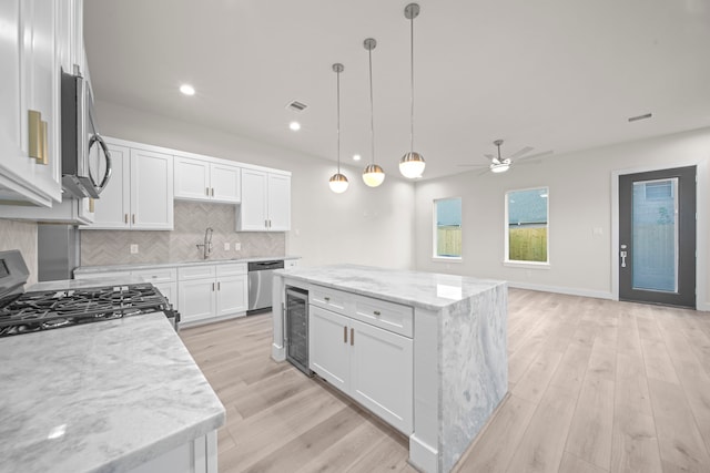 kitchen featuring white cabinets, hanging light fixtures, stainless steel appliances, and light hardwood / wood-style floors