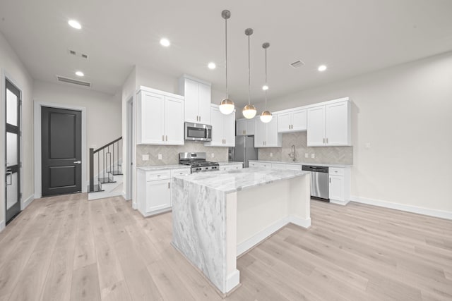 kitchen with an island with sink, stainless steel appliances, light stone countertops, light wood-type flooring, and white cabinets