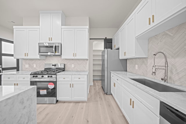 kitchen featuring a barn door, stainless steel appliances, light wood-type flooring, and white cabinets