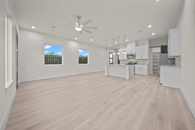 unfurnished living room with a barn door, light wood-type flooring, and ceiling fan