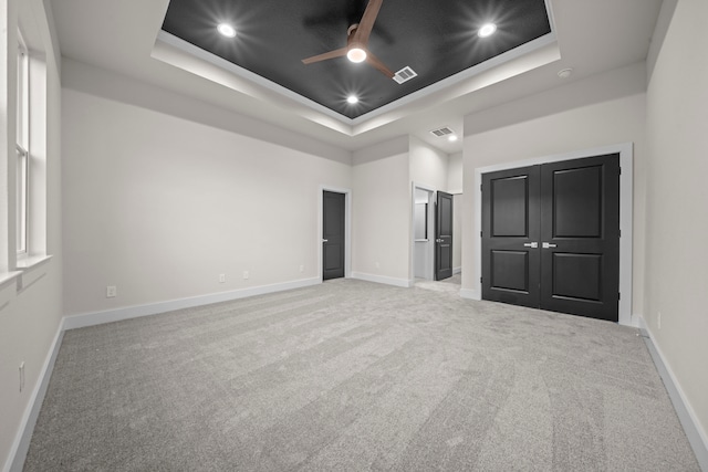 unfurnished bedroom with ceiling fan, a raised ceiling, and light colored carpet