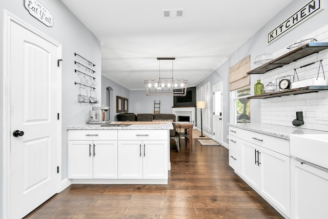 kitchen featuring decorative backsplash, white cabinetry, a fireplace, dark hardwood / wood-style flooring, and pendant lighting