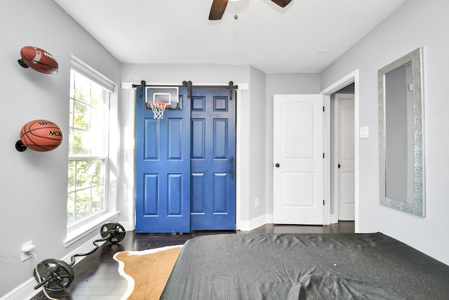 unfurnished bedroom featuring a barn door, dark wood-type flooring, and ceiling fan