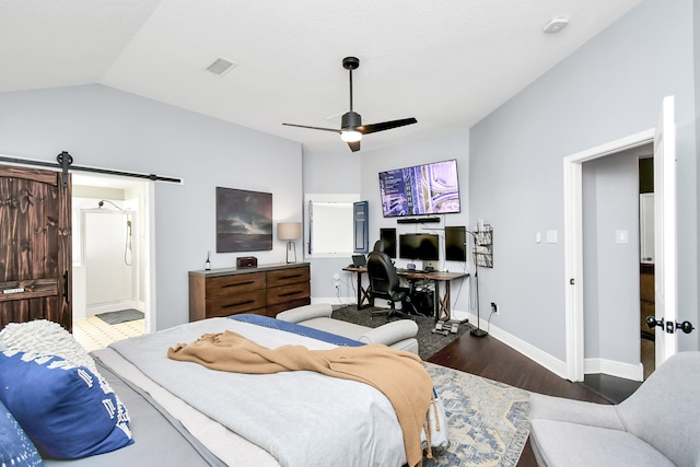 bedroom featuring vaulted ceiling, dark wood-type flooring, a barn door, connected bathroom, and ceiling fan