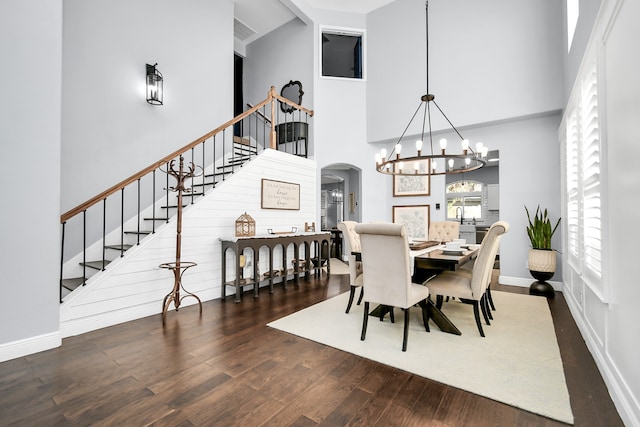 dining area with a towering ceiling, dark wood-type flooring, and a chandelier