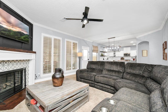 living room with a tile fireplace, ornamental molding, sink, and ceiling fan