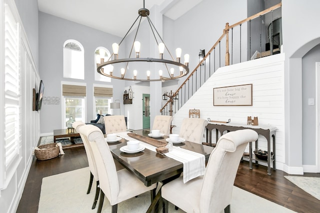 dining space with an inviting chandelier, a towering ceiling, and dark wood-type flooring