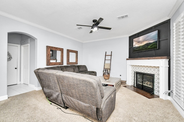 carpeted living room with ceiling fan, a textured ceiling, a fireplace, and ornamental molding