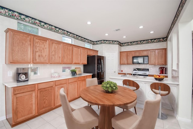 kitchen featuring black appliances, a kitchen breakfast bar, light tile patterned flooring, and backsplash