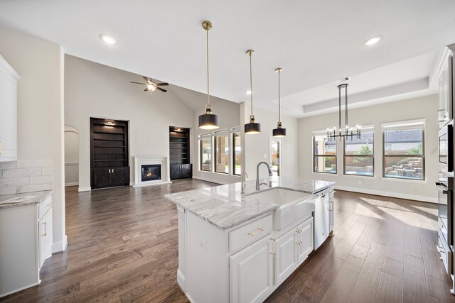 kitchen with light stone counters, dark wood-type flooring, a kitchen island with sink, sink, and white cabinetry