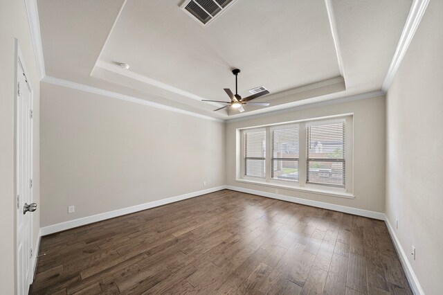 empty room with a tray ceiling, dark hardwood / wood-style floors, and crown molding