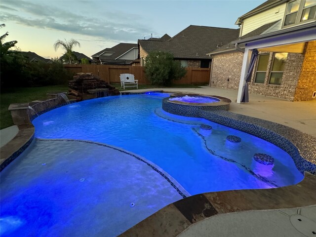 pool at dusk with pool water feature, an in ground hot tub, and a patio area