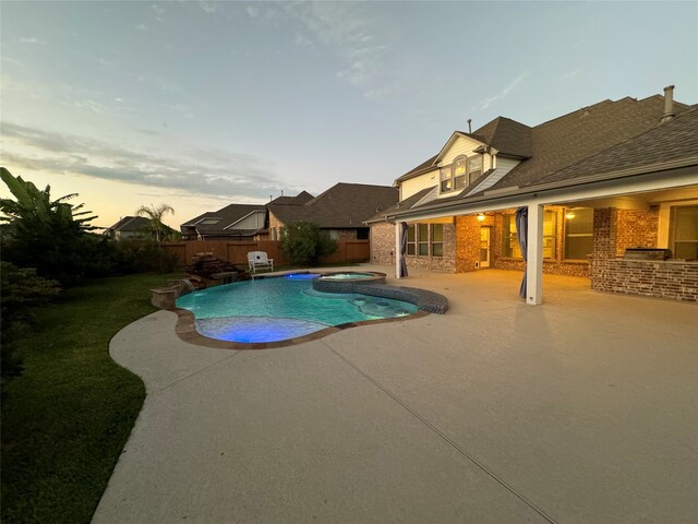 pool at dusk with an in ground hot tub and a patio area