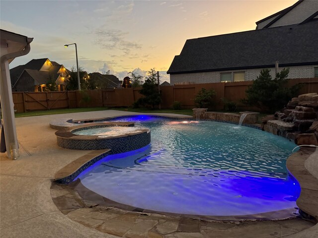 pool at dusk with pool water feature, an in ground hot tub, and a patio area