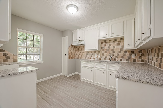 kitchen with light wood-type flooring, light stone counters, sink, white cabinets, and decorative backsplash