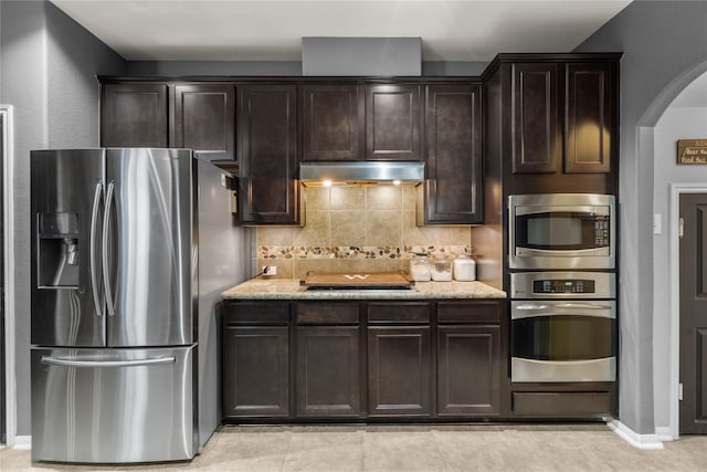 kitchen featuring decorative backsplash, dark brown cabinets, appliances with stainless steel finishes, and light stone countertops