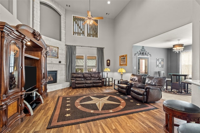 living room featuring high vaulted ceiling, ceiling fan with notable chandelier, hardwood / wood-style flooring, and a stone fireplace