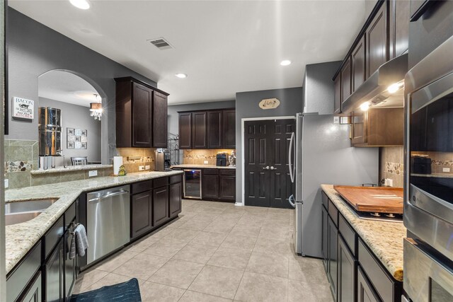 kitchen featuring appliances with stainless steel finishes, decorative backsplash, light stone counters, light tile patterned floors, and dark brown cabinetry