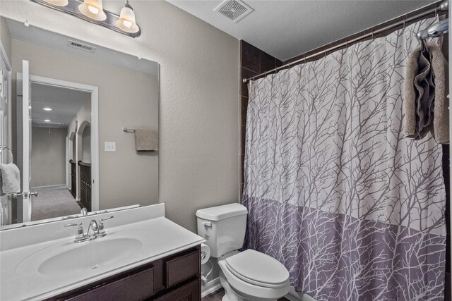 bathroom featuring a textured ceiling, curtained shower, vanity, and toilet