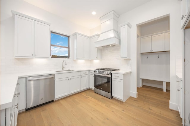 kitchen with white cabinets, appliances with stainless steel finishes, premium range hood, backsplash, and sink