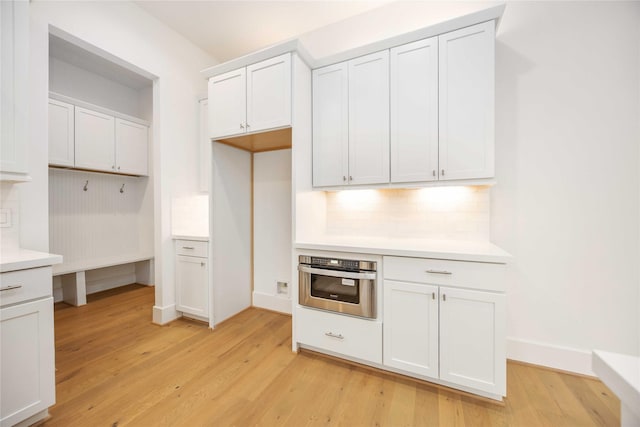 kitchen featuring light hardwood / wood-style floors, white cabinetry, stainless steel oven, and tasteful backsplash