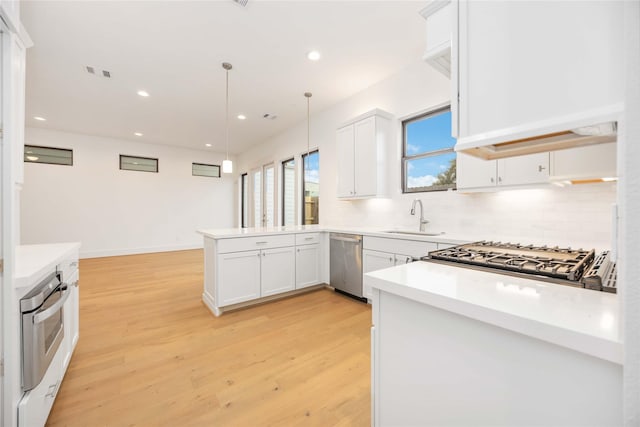 kitchen featuring appliances with stainless steel finishes, decorative light fixtures, white cabinetry, sink, and kitchen peninsula