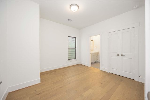 unfurnished bedroom featuring a closet, connected bathroom, and light hardwood / wood-style flooring