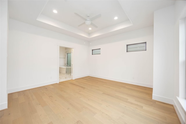 empty room with light hardwood / wood-style floors, a tray ceiling, and ceiling fan