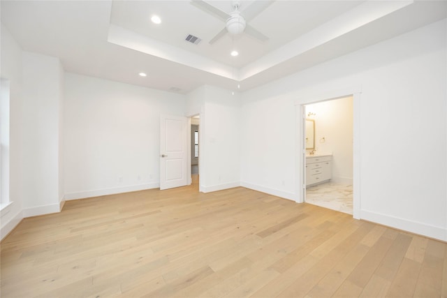 unfurnished bedroom featuring ceiling fan, a raised ceiling, ensuite bath, and light wood-type flooring