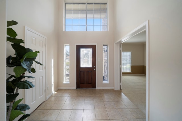 foyer with ornamental molding, light carpet, a towering ceiling, and plenty of natural light