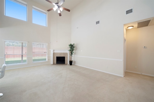 unfurnished living room with light carpet, a tile fireplace, a high ceiling, and ceiling fan