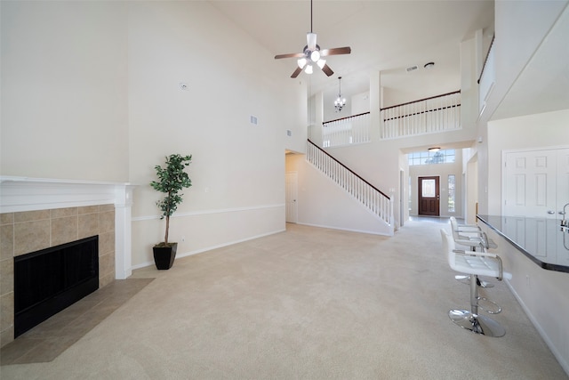 carpeted living room with a towering ceiling, a tile fireplace, and ceiling fan with notable chandelier