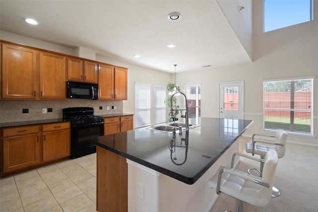 kitchen featuring plenty of natural light, black appliances, decorative light fixtures, and an island with sink