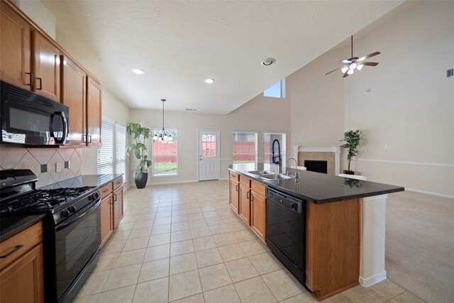 kitchen with light tile patterned floors, an island with sink, black appliances, sink, and decorative light fixtures