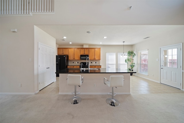 kitchen with a center island with sink, black appliances, light colored carpet, and a breakfast bar