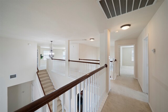 hallway with a notable chandelier and light colored carpet