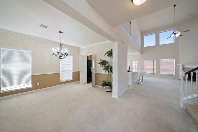 empty room featuring light carpet, ornamental molding, a high ceiling, and ceiling fan with notable chandelier