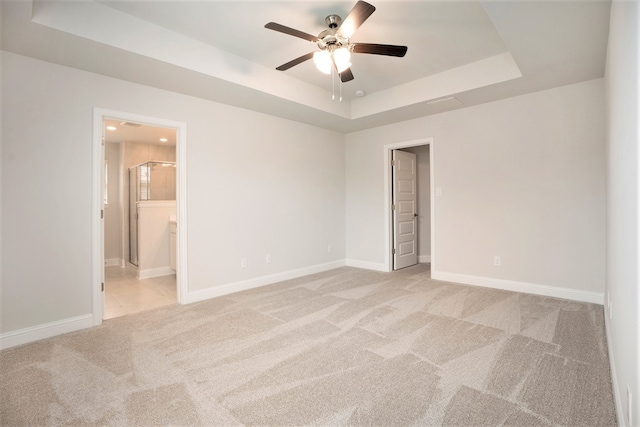 empty room with a raised ceiling, ceiling fan, and light colored carpet