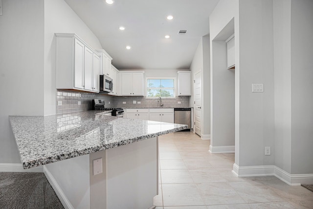 kitchen with appliances with stainless steel finishes, white cabinets, kitchen peninsula, light stone countertops, and sink