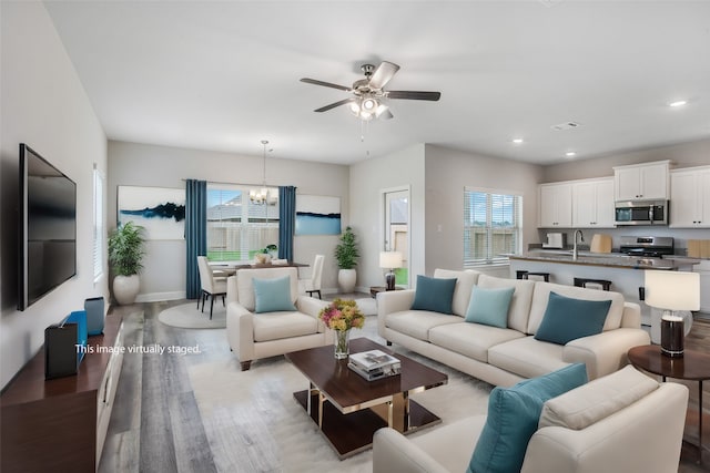 living room with ceiling fan with notable chandelier, light hardwood / wood-style floors, and sink