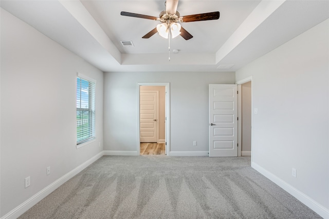 unfurnished bedroom with light carpet, a tray ceiling, and ceiling fan