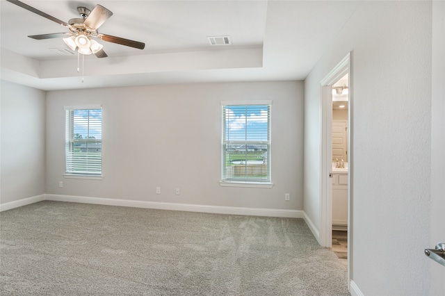 carpeted empty room with a raised ceiling, ceiling fan, and a wealth of natural light